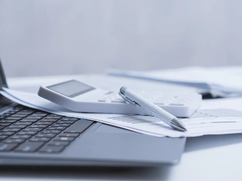 Laptop, calculator, pen, and accounting documents on a desk